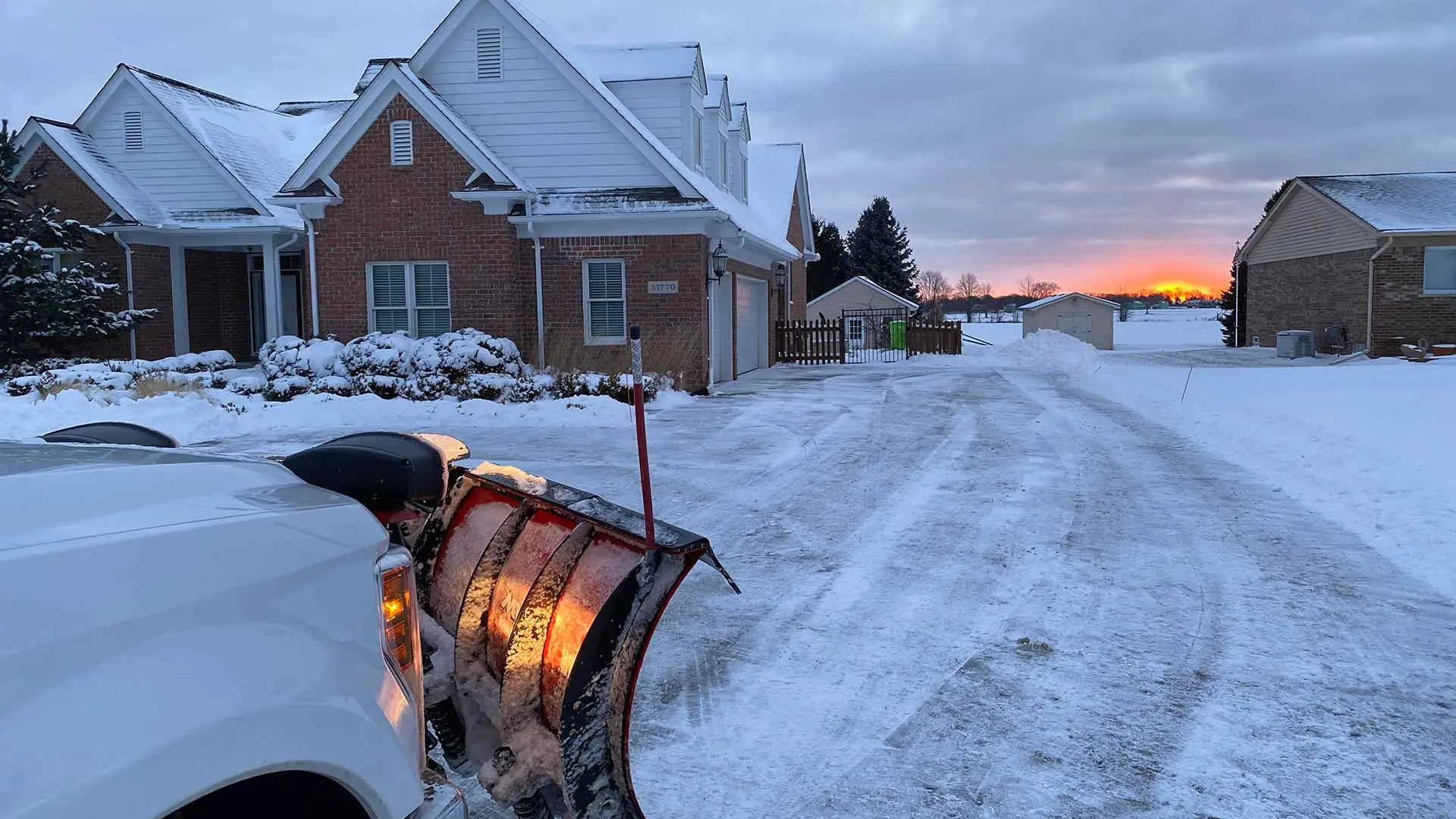 Truck with snow plow clearing snow at a Macomb, MI home at sunrise.