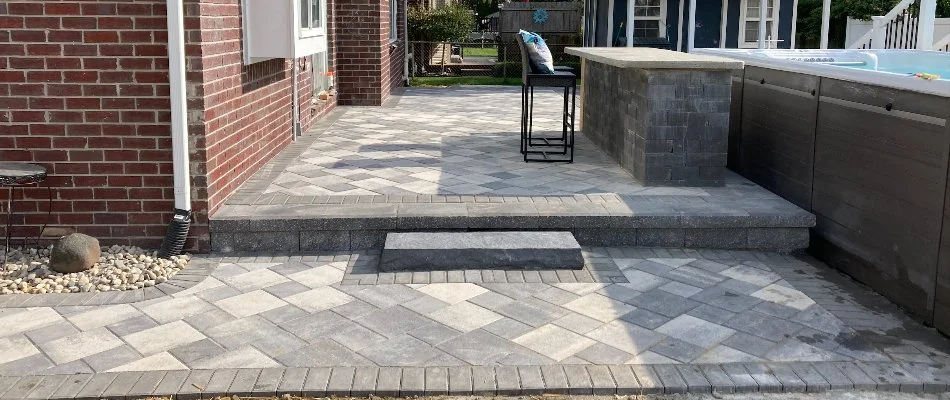 A backyard paver patio in Macomb, MI, installed near a brick home and an above-ground pool.