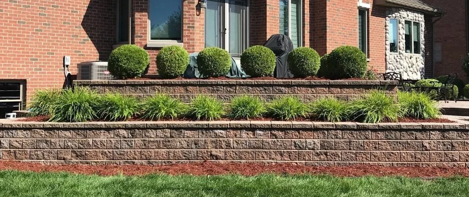 A brick retaining wall in a backyard in Macomb, MI, with mulch beds and shrubs.