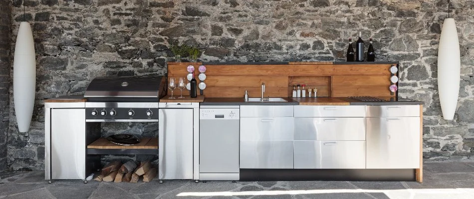 Stone outdoor kitchen in Macomb, MI, with a grill, sink, and stainless steel drawers.