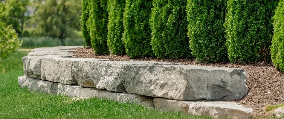 Stone retaining wall in Macomb, MI, with green shrubs.