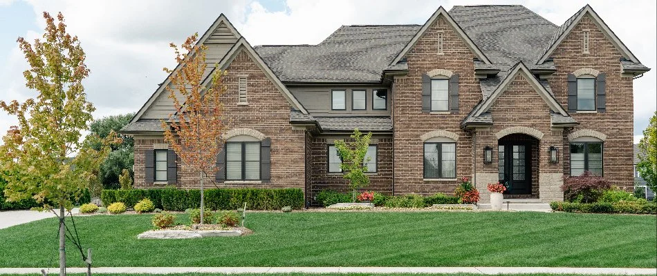 Close-up view of the entryway of a brick house surrounded by a beautifully landscaped garden with colorful flowers and greenery