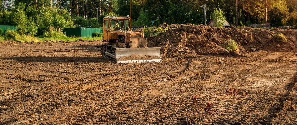 Dirt lot in Macomb, MI, with a tractor and vegetation.